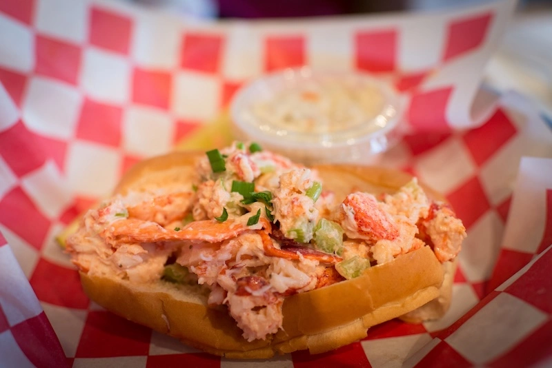 Lobster roll filled with chunky lobster meat, green onions, and celery in a buttery split-top bun, served with coleslaw.