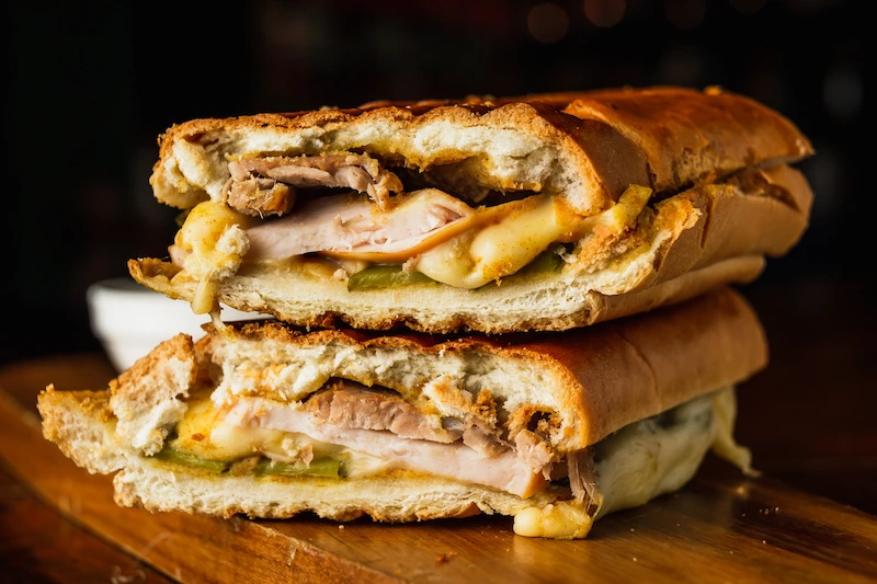 A stacked Cuban medianoche sandwich with roast pork, ham, melted Swiss cheese, pickles, and mustard, pressed between sweet, golden bread.