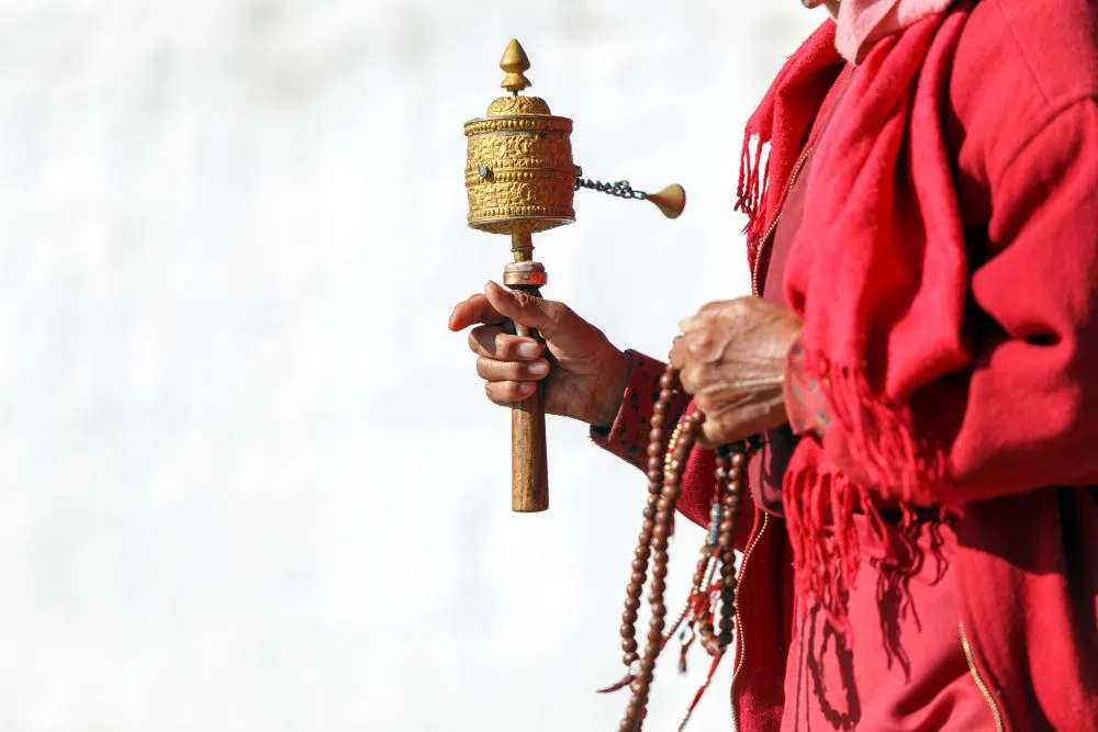 Bhutanese monk holding a golden prayer wheel and meditation beads in traditional red robes