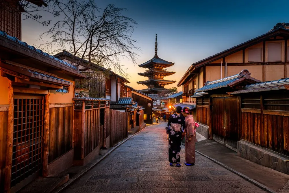 Women in traditional kimonos walking through Higashiyama district at sunset with Yasaka Pagoda in Kyoto, Japan
