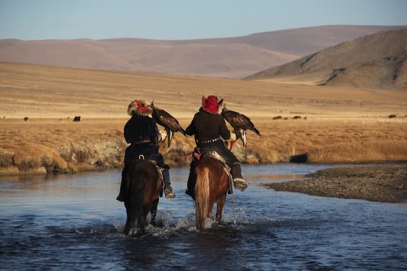 Kazakh eagle hunters on horseback crossing a river in western Mongolia