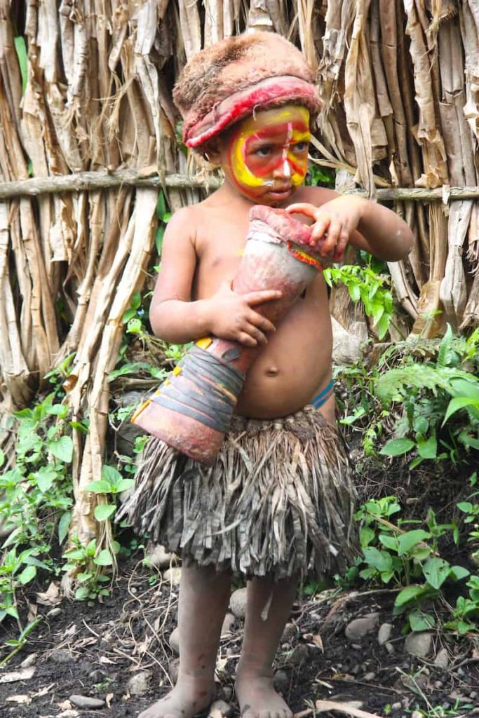 Child wearing traditional face paint and grass skirt in a Papua New Guinea highland village