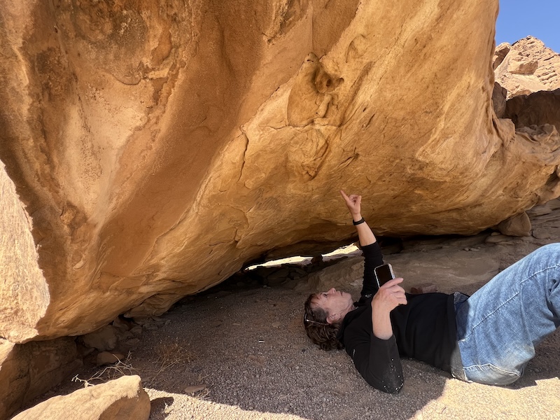 Field study participant observing sedimentary rock formations in a desert landscape.