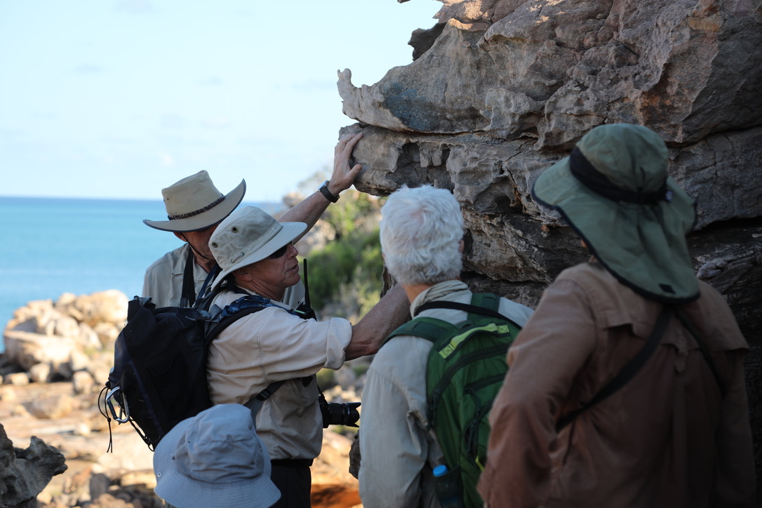 A guide explains coastal rock formations to a small group during a field-based educational excursion.