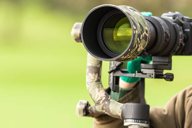 Bird photography lens mounted on gimbal head in field, camouflage wrap on telephoto