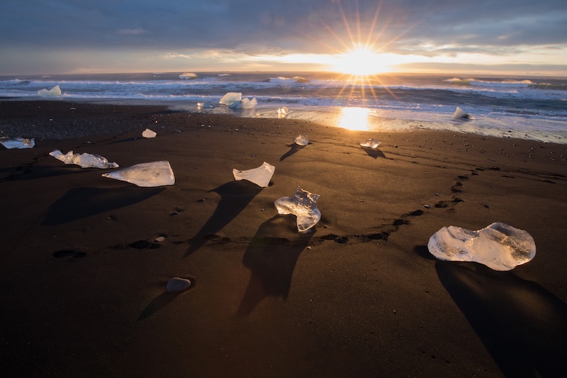 Glittering iceberg fragments scattered across the black volcanic sand of Diamond Beach at sunrise
