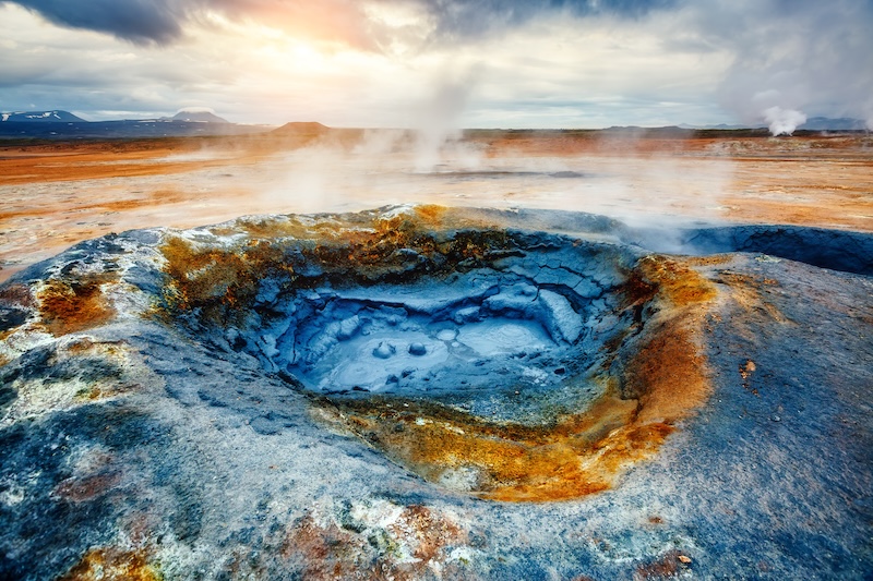 Steaming mineral-rich mud pool at the Hverir geothermal area near Lake Mývatn, surrounded by orange sulfuric earth