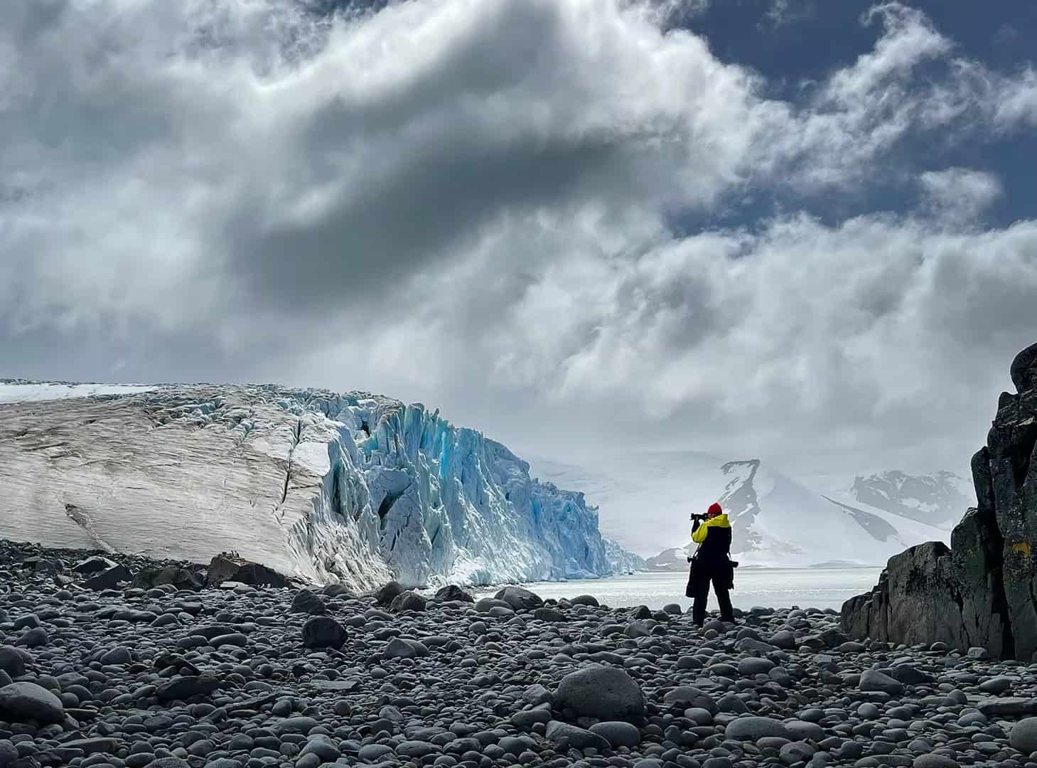 Michelle Valberg photographing a glacier from a rocky beach in Antarctica