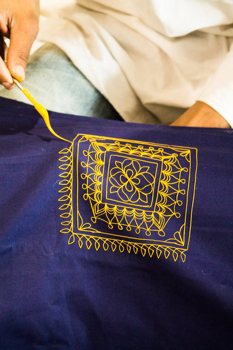 Artisan hand-painting a traditional Rogan art design with yellow paint on indigo fabric in Kutch, Gujarat