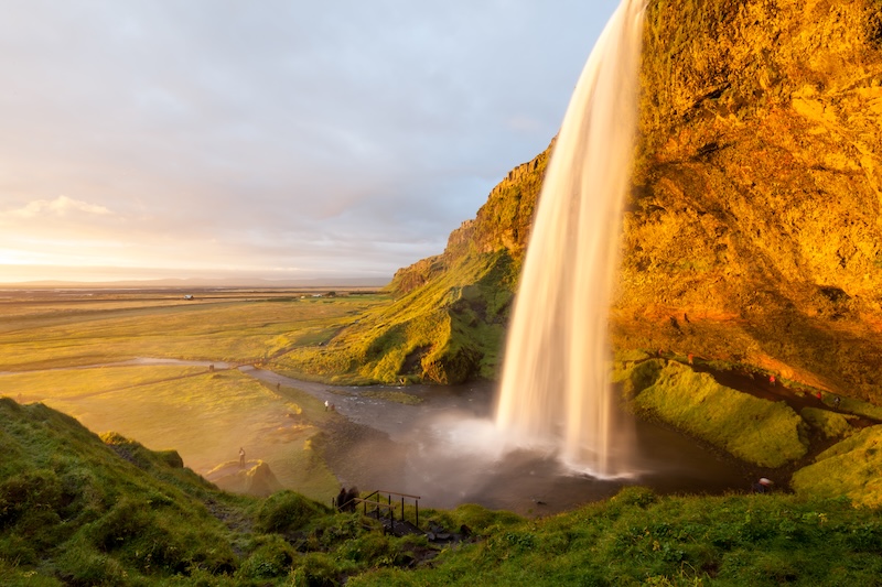 Seljalandsfoss waterfall glowing gold at sunset, with the path behind the falls visible on Iceland's South Coast
